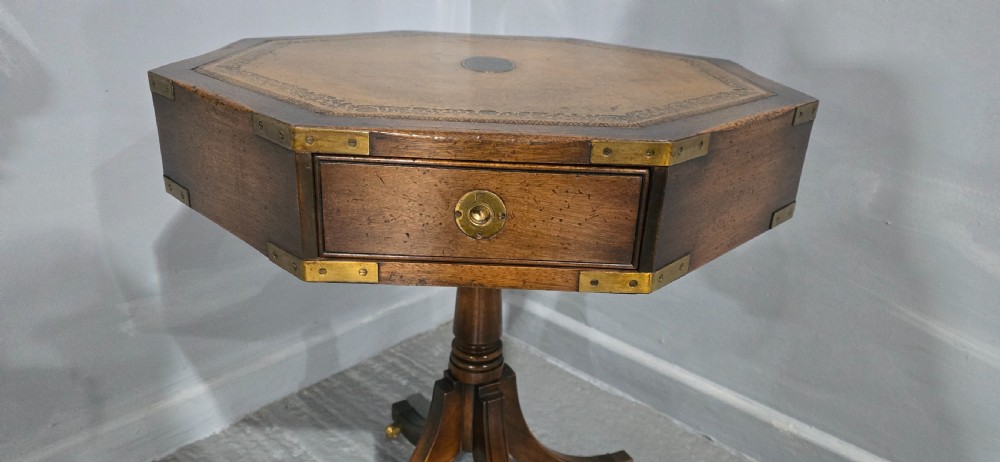 An octagonal mahogany campaign drum table with a gilt-tooled brown leather insert top, brass corner mounts, a single frieze drawer, and a four-legged pedestal base with brass castors. View IV