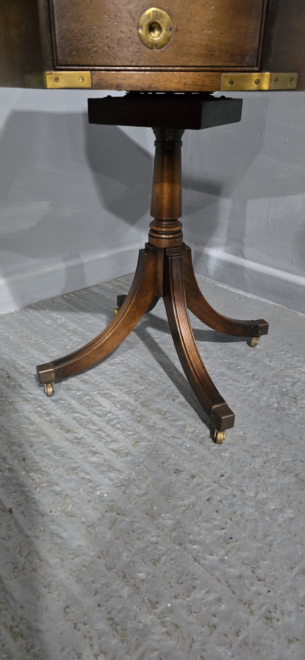 An octagonal mahogany campaign drum table with a gilt-tooled brown leather insert top, brass corner mounts, a single frieze drawer, and a four-legged pedestal base with brass castors. View V