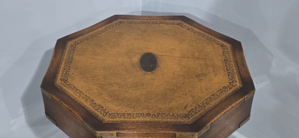 An octagonal mahogany campaign drum table with a gilt-tooled brown leather insert top, brass corner mounts, a single frieze drawer, and a four-legged pedestal base with brass castors. View VI