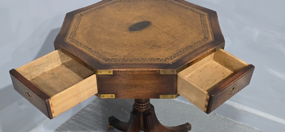 An octagonal mahogany campaign drum table with a gilt-tooled brown leather insert top, brass corner mounts, a single frieze drawer, and a four-legged pedestal base with brass castors. View VIII