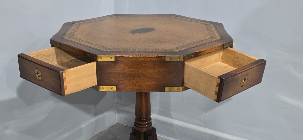 An octagonal mahogany campaign drum table with a gilt-tooled brown leather insert top, brass corner mounts, a single frieze drawer, and a four-legged pedestal base with brass castors. View IX