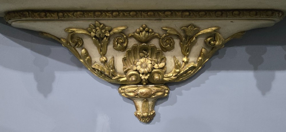An antique French cream and gold painted wall vitrine featuring a central arched glazed door, open side shelves backed with red velvet, and carved gilt accents. View VII