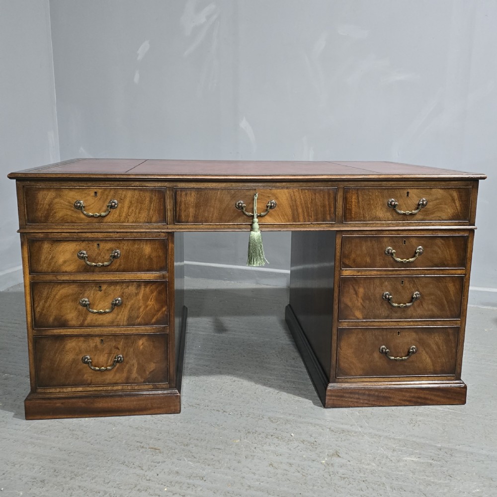 A double-pedestal mahogany partners desk featuring a leather-inset writing surface and brass swan-neck handles on multiple drawers.