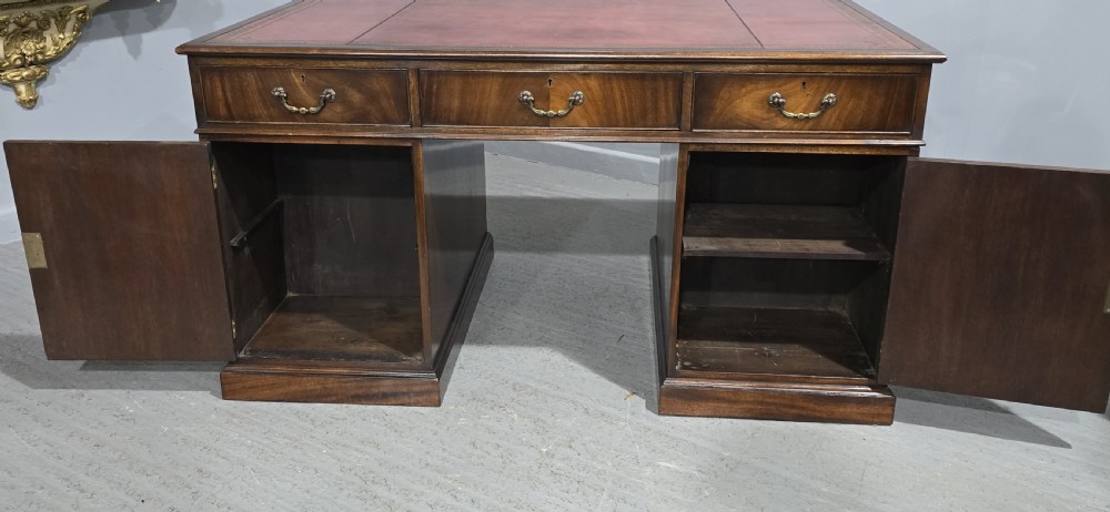 A double-pedestal mahogany partners desk featuring a leather-inset writing surface and brass swan-neck handles on multiple drawers. View XII