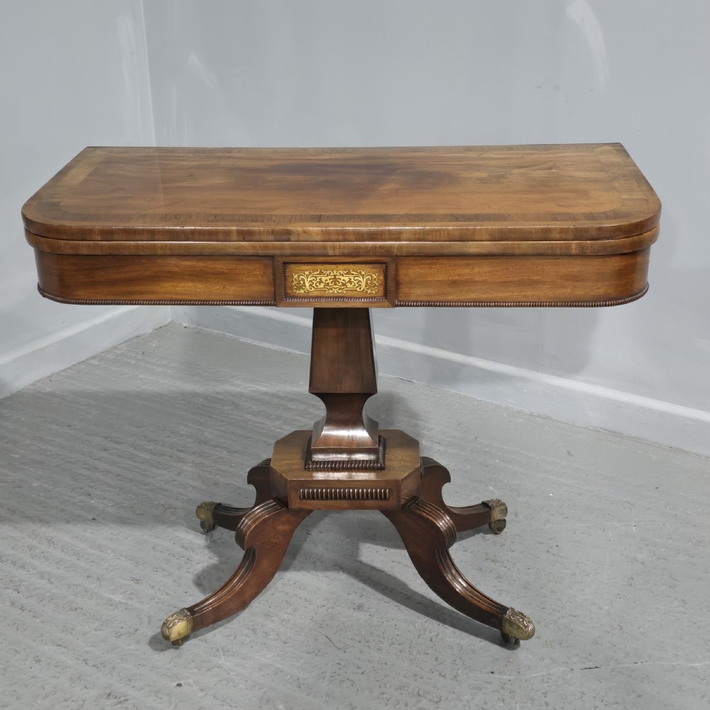 A Regency brass inlaid wooden card table featuring a fold-over top, central pedestal column, and four splayed legs with brass paw feet.
