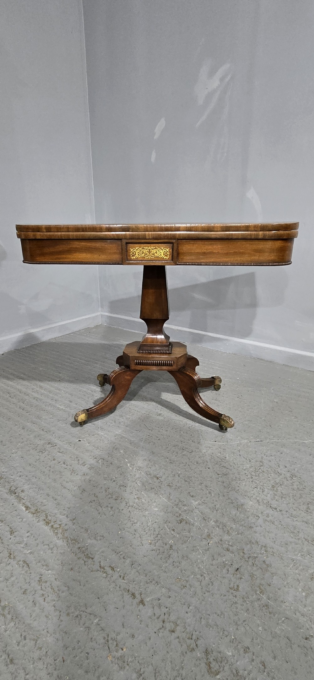 A Regency brass inlaid wooden card table featuring a fold-over top, central pedestal column, and four splayed legs with brass paw feet. View VII