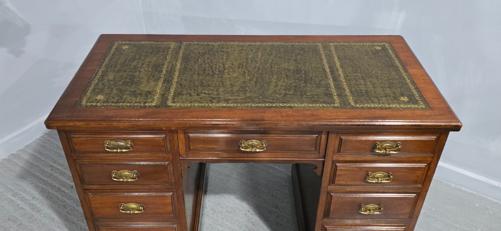 A warm brown mahogany pedestal desk featuring a green leather writing top, nine drawers, and brass swan-neck handles set upon twin plinth bases. View IV