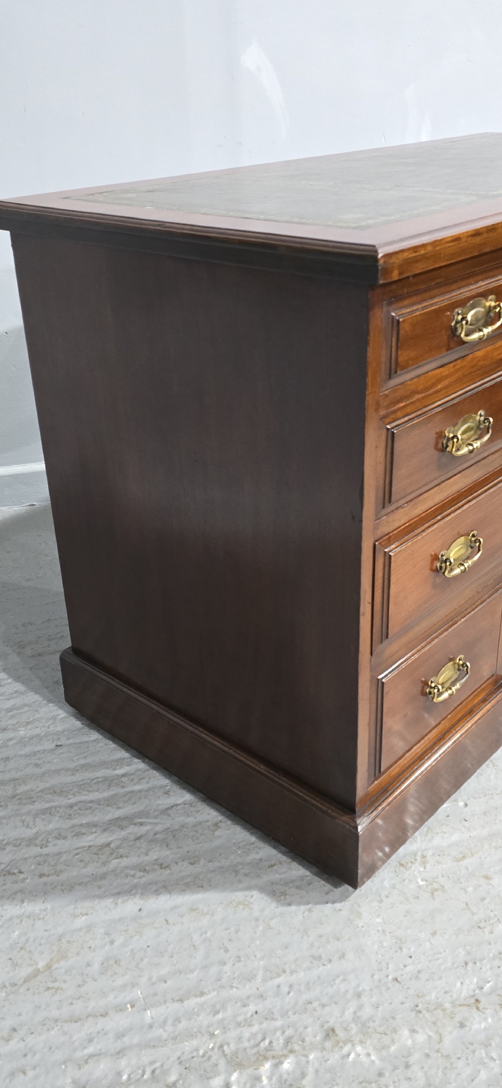 A warm brown mahogany pedestal desk featuring a green leather writing top, nine drawers, and brass swan-neck handles set upon twin plinth bases. View V