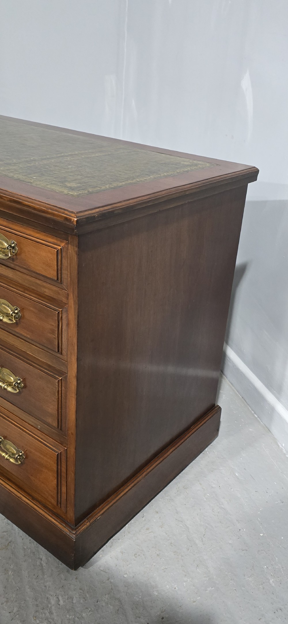 A warm brown mahogany pedestal desk featuring a green leather writing top, nine drawers, and brass swan-neck handles set upon twin plinth bases. View VI