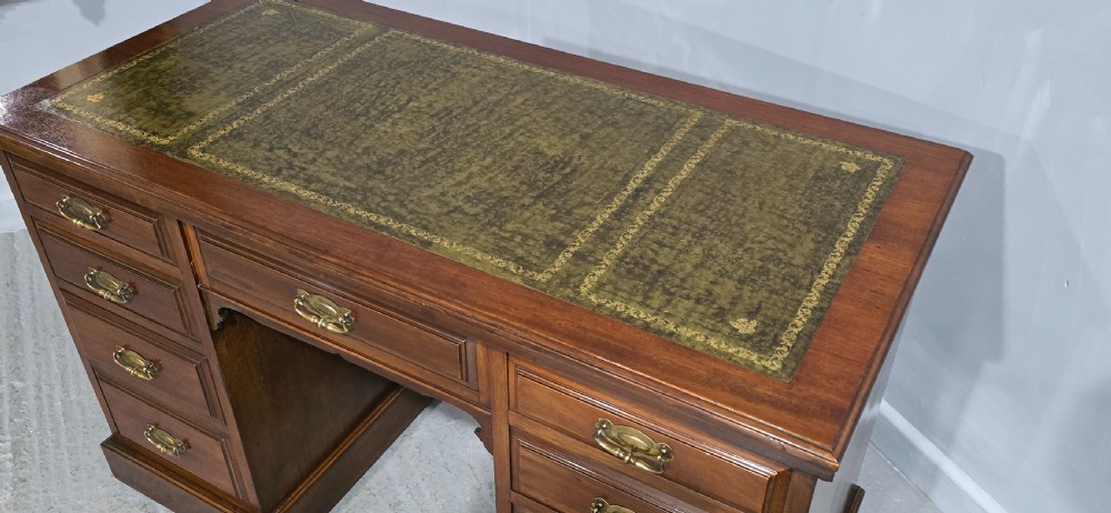 A warm brown mahogany pedestal desk featuring a green leather writing top, nine drawers, and brass swan-neck handles set upon twin plinth bases. View VII