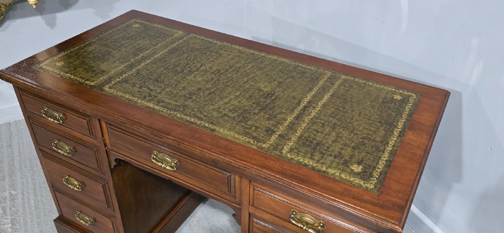 A warm brown mahogany pedestal desk featuring a green leather writing top, nine drawers, and brass swan-neck handles set upon twin plinth bases. View VIII