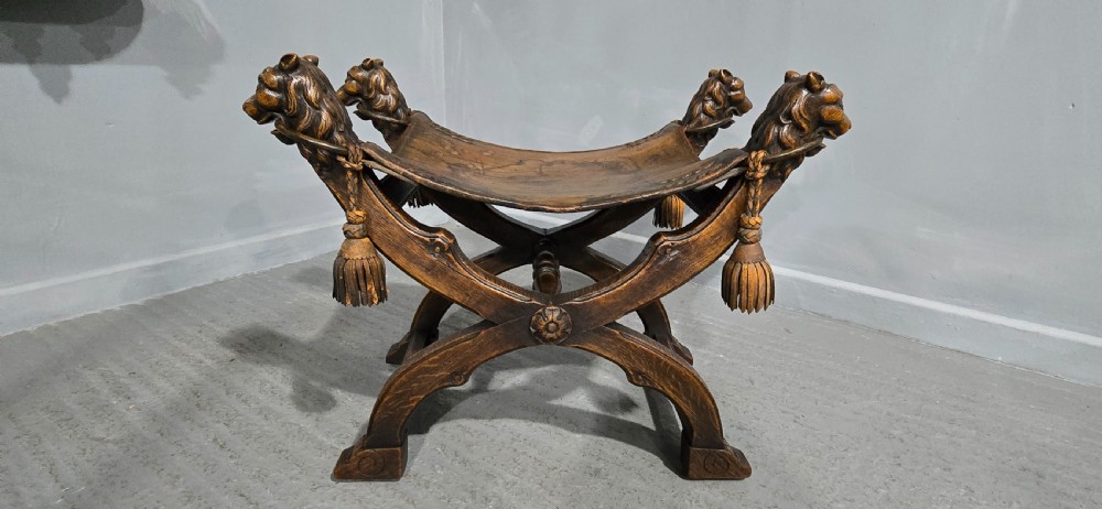 A carved dark walnut X-frame curule stool featuring lion heads with carved wooden tassels at the top corners and a slung brown leather seat. View III