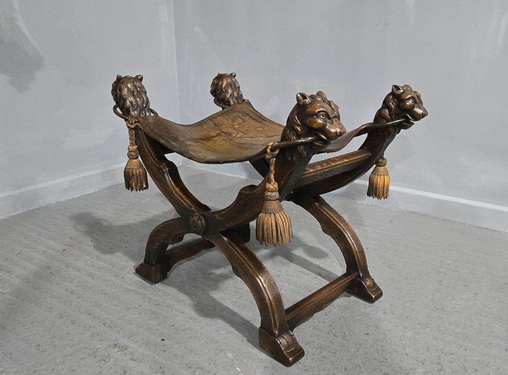 A carved dark walnut X-frame curule stool featuring lion heads with carved wooden tassels at the top corners and a slung brown leather seat. View IV