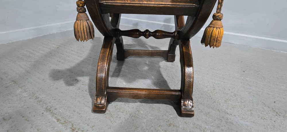 A carved dark walnut X-frame curule stool featuring lion heads with carved wooden tassels at the top corners and a slung brown leather seat. View IX