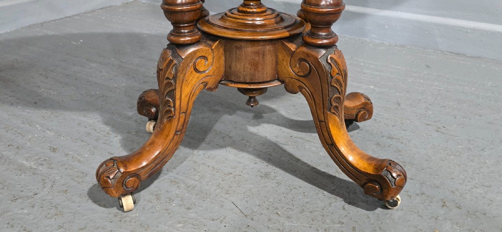An oval Victorian centre table made from burr walnut with floral marquetry inlay, four turned support columns, and carved legs on castors. View III