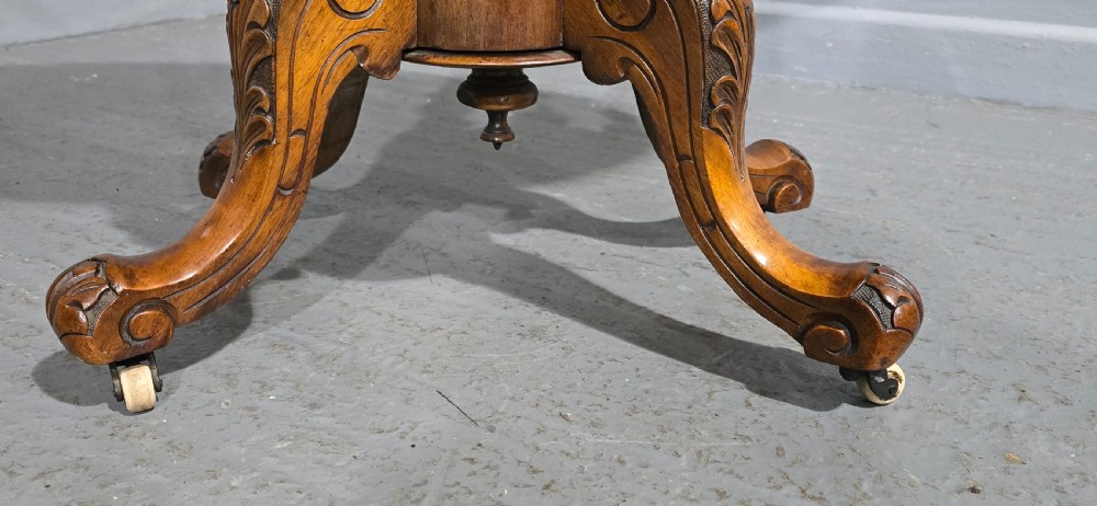 An oval Victorian centre table made from burr walnut with floral marquetry inlay, four turned support columns, and carved legs on castors. View IV