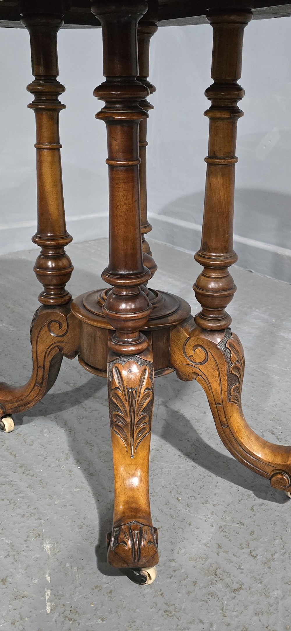 An oval Victorian centre table made from burr walnut with floral marquetry inlay, four turned support columns, and carved legs on castors. View V