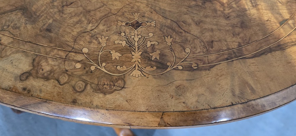 An oval Victorian centre table made from burr walnut with floral marquetry inlay, four turned support columns, and carved legs on castors. View VII