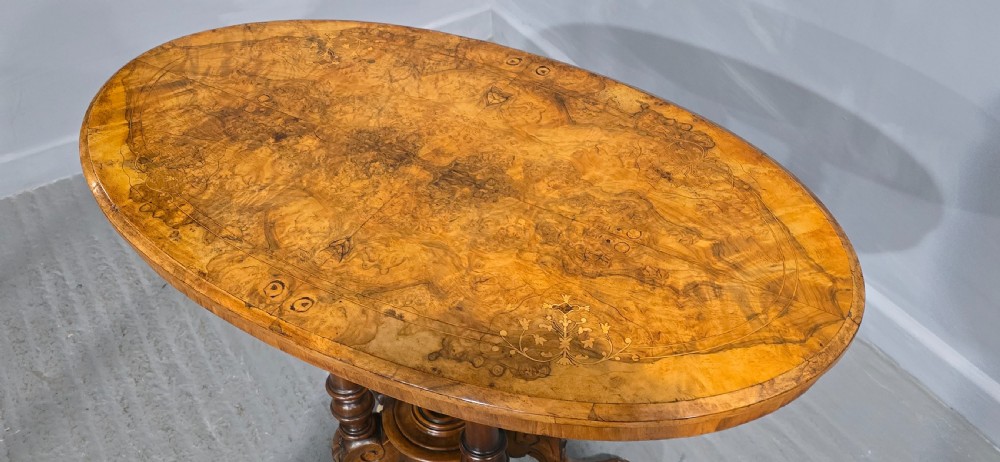 An oval Victorian centre table made from burr walnut with floral marquetry inlay, four turned support columns, and carved legs on castors. View VIII