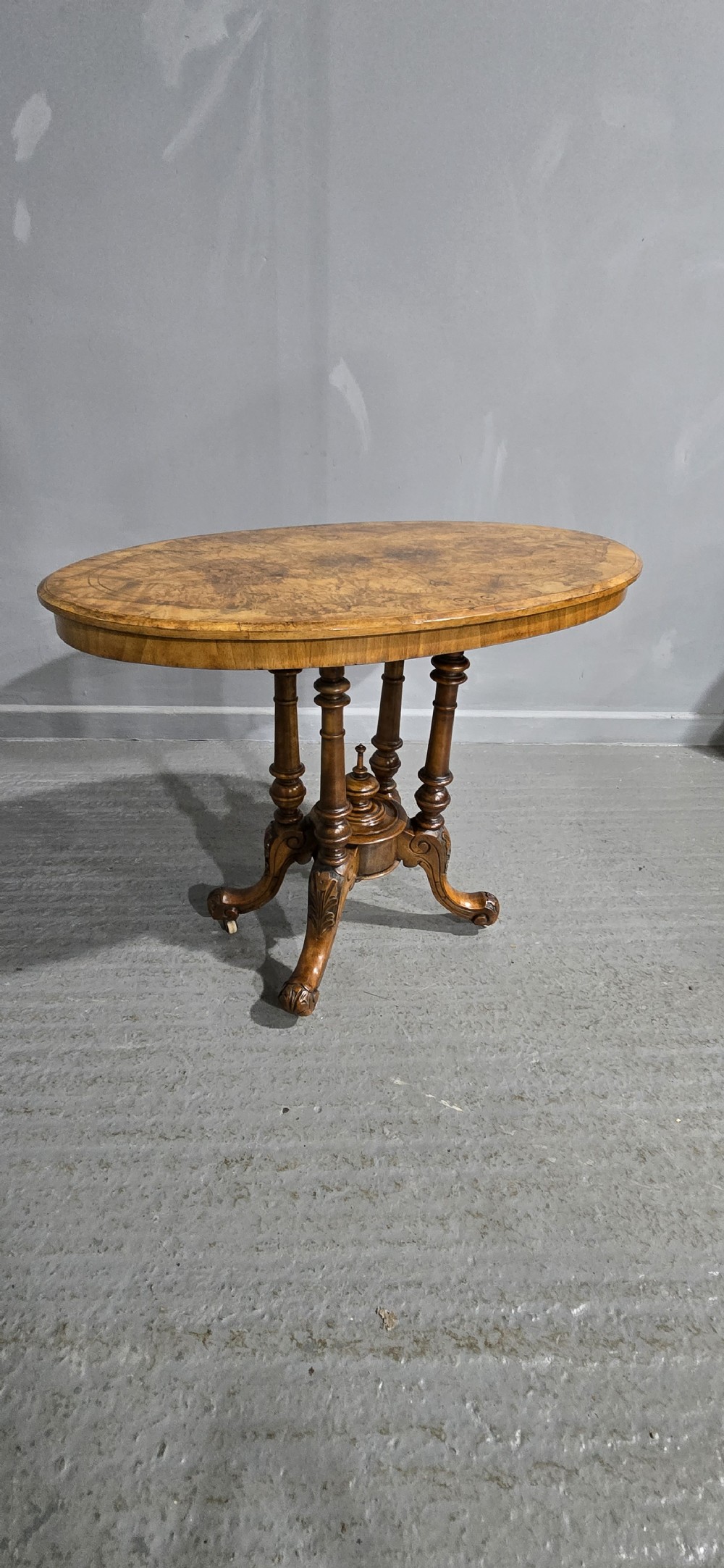 An oval Victorian centre table made from burr walnut with floral marquetry inlay, four turned support columns, and carved legs on castors. View X