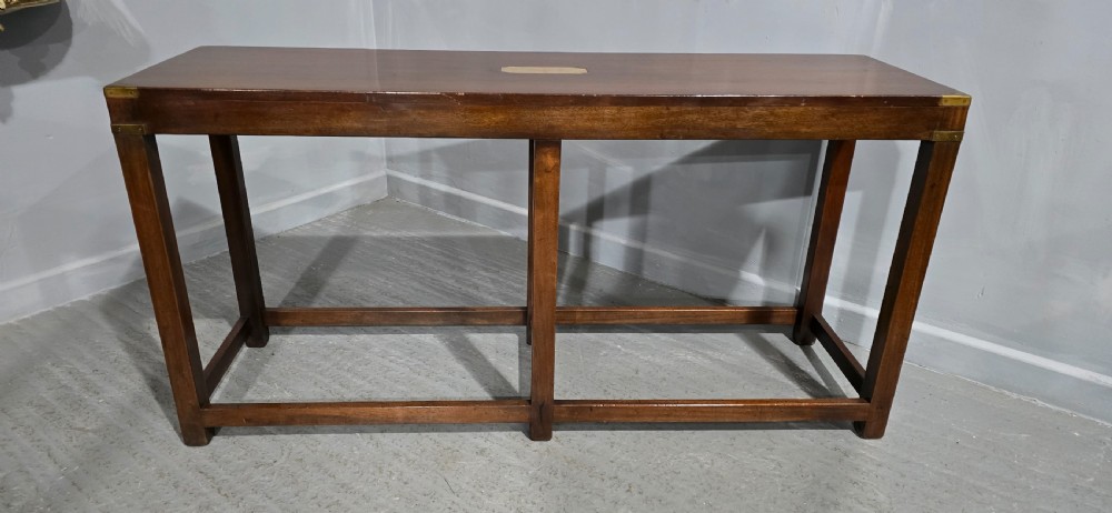 A rectangular mahogany campaign console table featuring brass corner mounts, an inset central brass plaque, and straight squared legs connected by a full box stretcher. View II