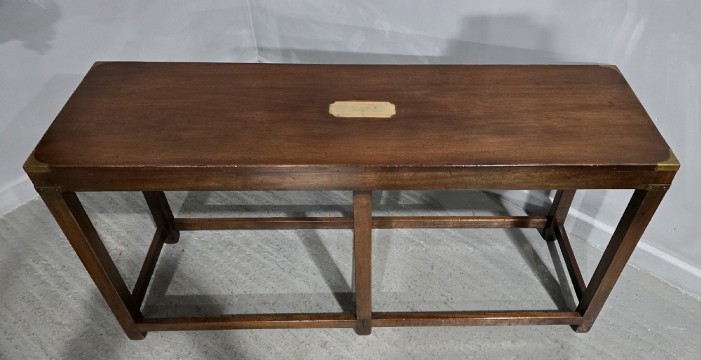 A rectangular mahogany campaign console table featuring brass corner mounts, an inset central brass plaque, and straight squared legs connected by a full box stretcher. View III
