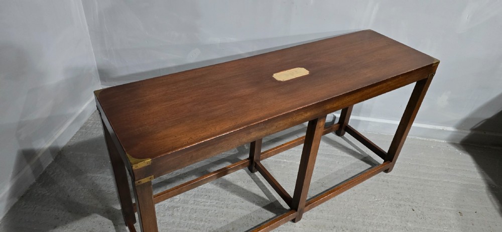 A rectangular mahogany campaign console table featuring brass corner mounts, an inset central brass plaque, and straight squared legs connected by a full box stretcher. View VII