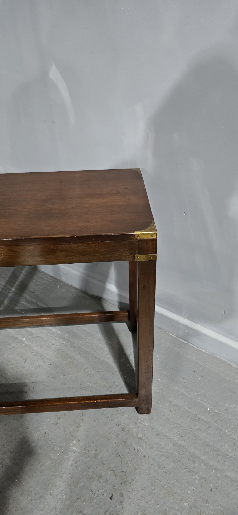 A rectangular mahogany campaign console table featuring brass corner mounts, an inset central brass plaque, and straight squared legs connected by a full box stretcher. View IX
