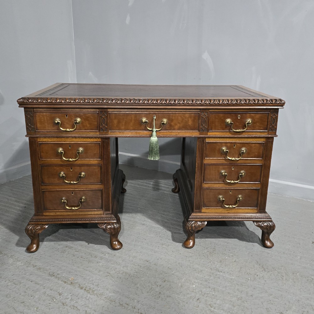 A Chippendale style mahogany pedestal desk featuring nine drawers with brass handles, a brown leather writing surface, and carved cabriole legs with ball-and-claw feet.