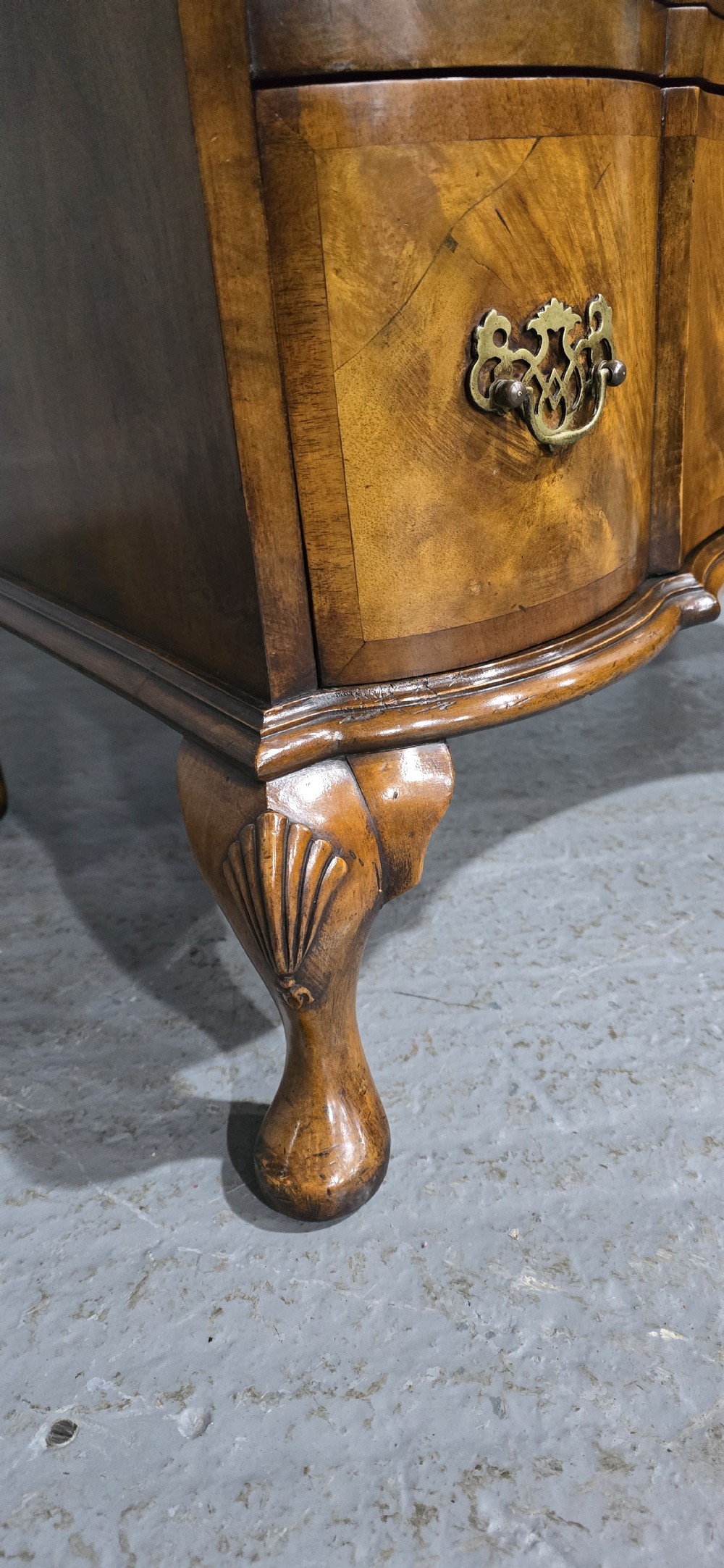 A four-drawer walnut chest of drawers featuring an inward-curving concave front, brass handles, and cabriole feet. View V