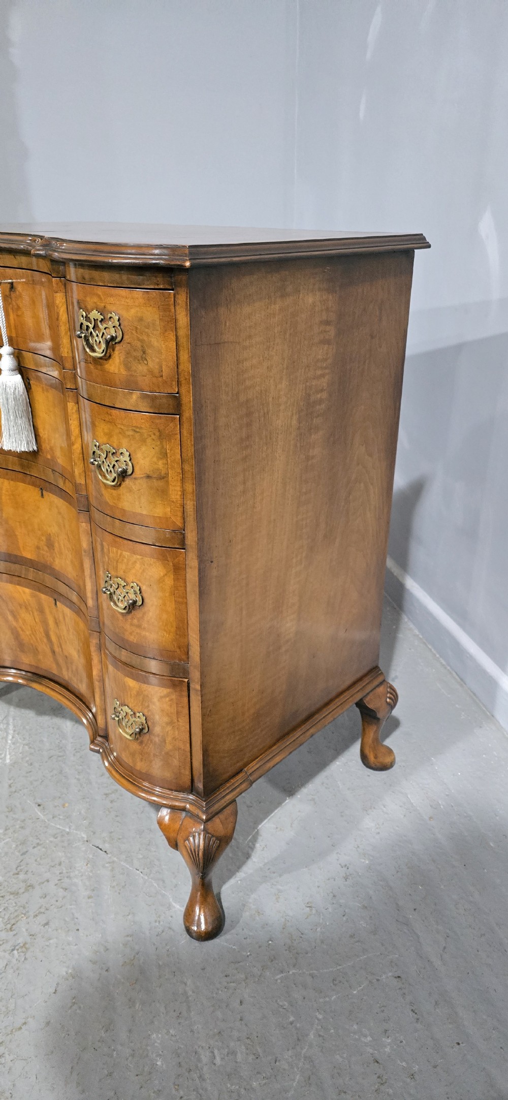 A four-drawer walnut chest of drawers featuring an inward-curving concave front, brass handles, and cabriole feet. View VII