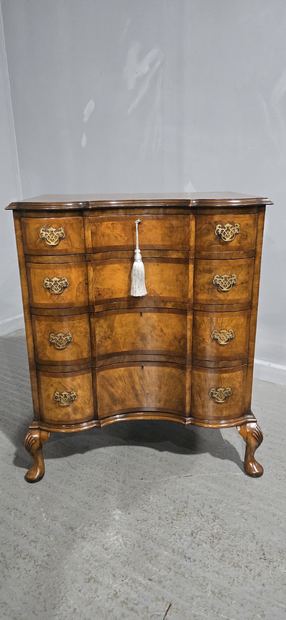 A four-drawer walnut chest of drawers featuring an inward-curving concave front, brass handles, and cabriole feet. View X
