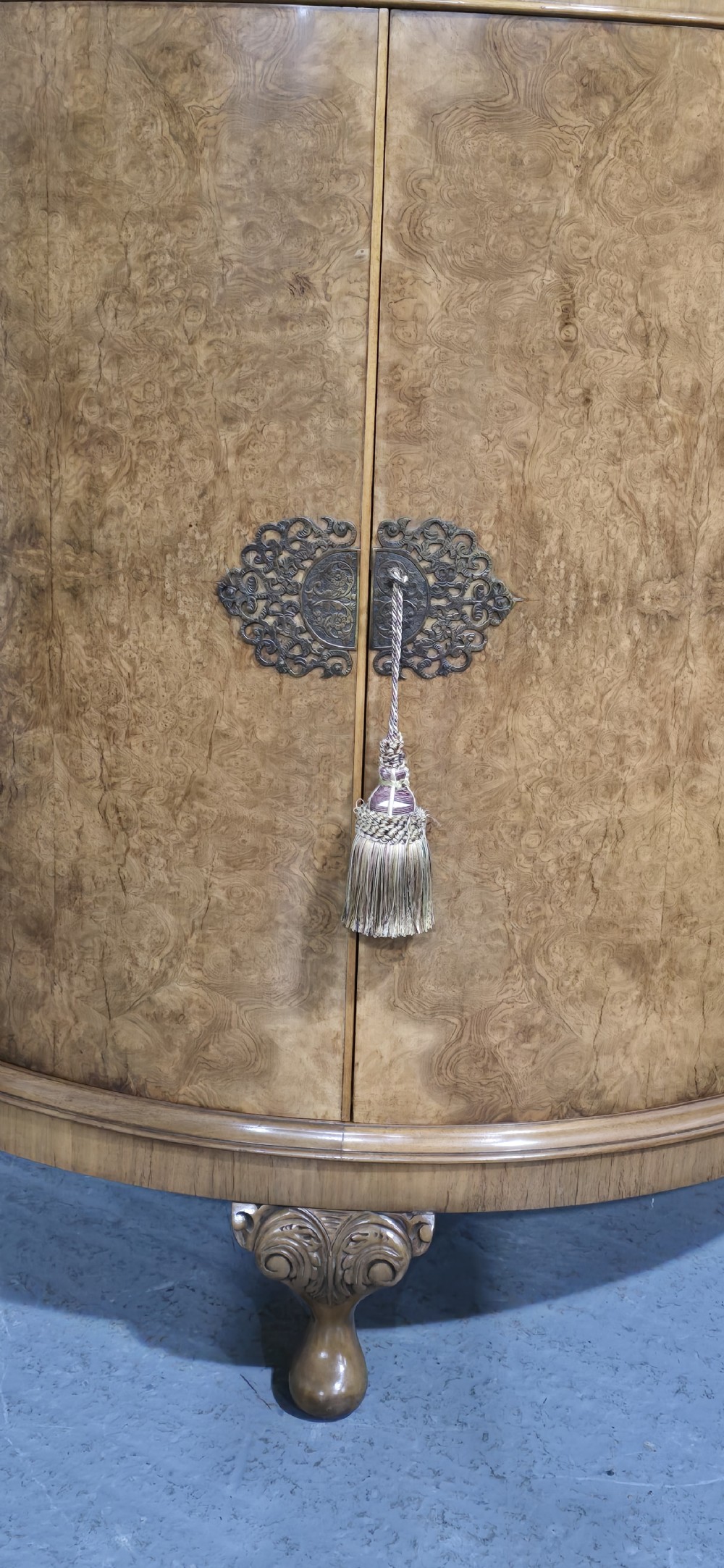 A semicircular burr walnut demi lune cabinet featuring double doors, figured wood grain, a central brass escutcheon with tassel, and carved cabriole legs. View II