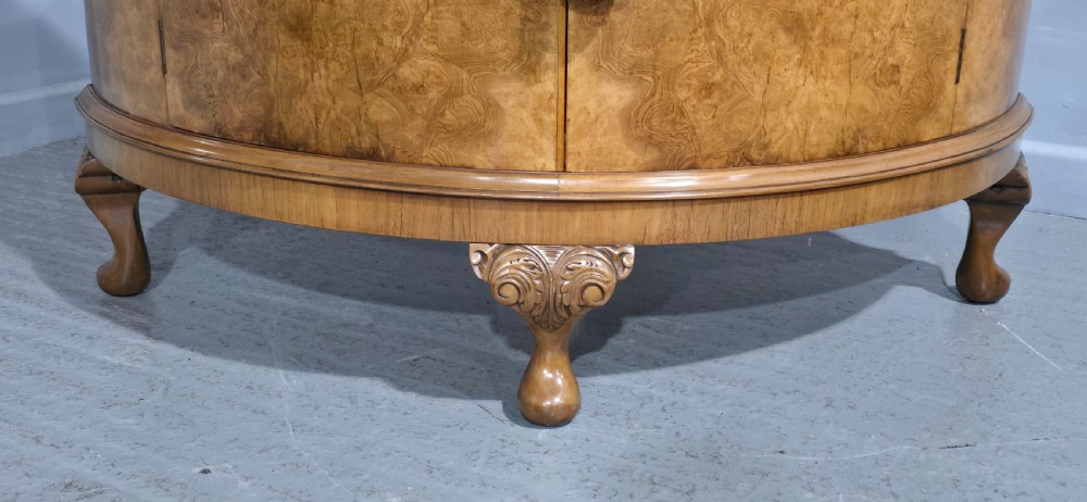 A semicircular burr walnut demi lune cabinet featuring double doors, figured wood grain, a central brass escutcheon with tassel, and carved cabriole legs. View IV