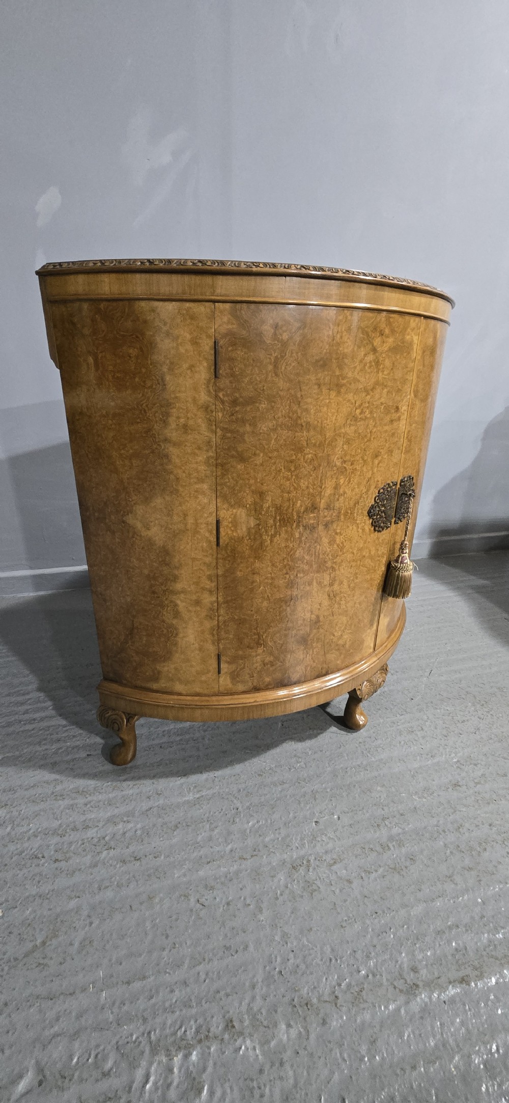 A semicircular burr walnut demi lune cabinet featuring double doors, figured wood grain, a central brass escutcheon with tassel, and carved cabriole legs. View V