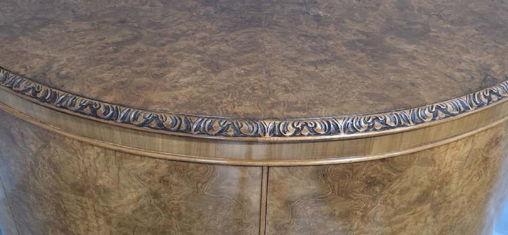 A semicircular burr walnut demi lune cabinet featuring double doors, figured wood grain, a central brass escutcheon with tassel, and carved cabriole legs. View VII