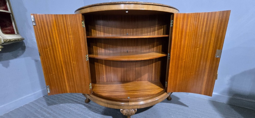 A semicircular burr walnut demi lune cabinet featuring double doors, figured wood grain, a central brass escutcheon with tassel, and carved cabriole legs. View VIII