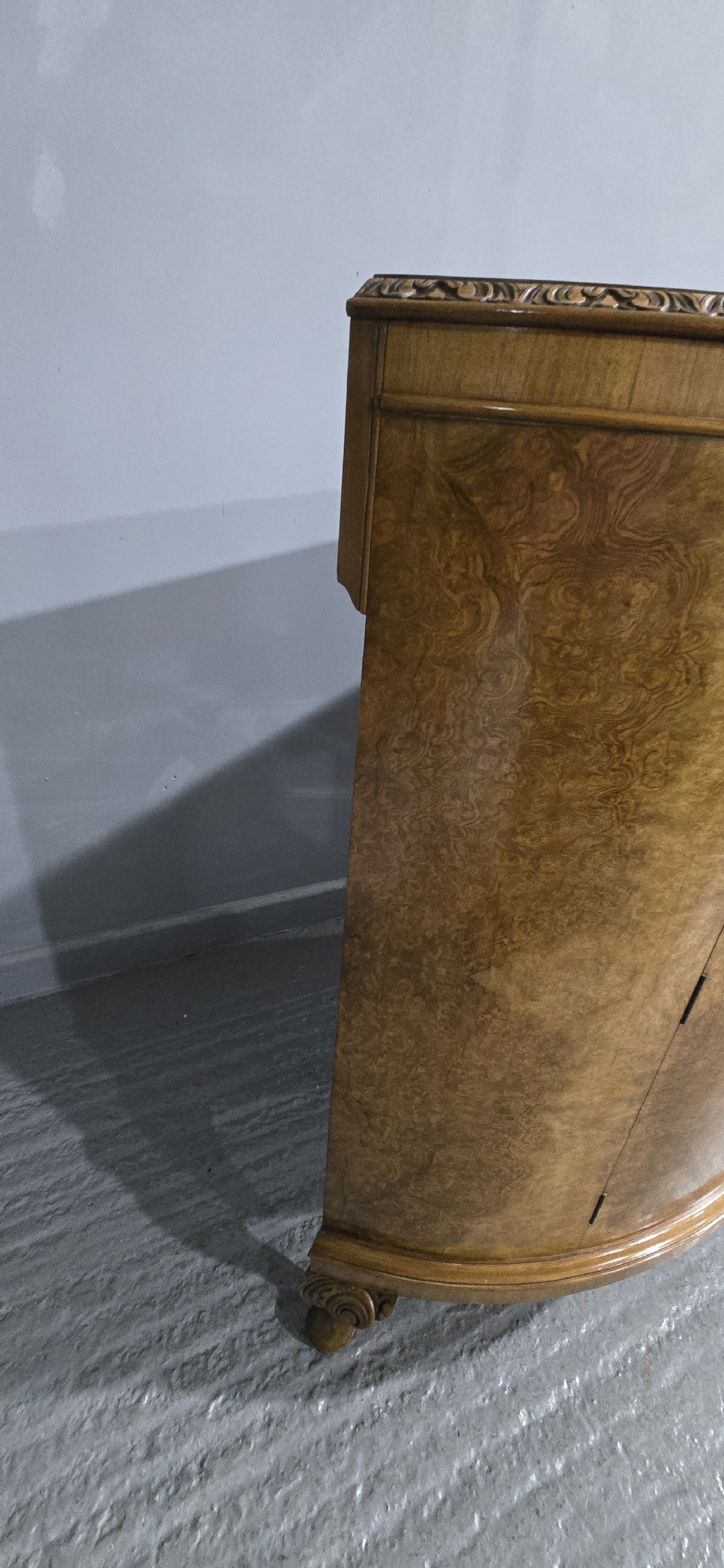 A semicircular burr walnut demi lune cabinet featuring double doors, figured wood grain, a central brass escutcheon with tassel, and carved cabriole legs. View X
