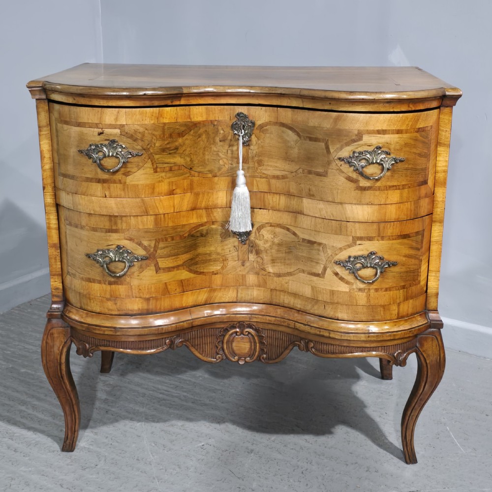 An antique walnut commode featuring two drawers with serpentine fronts, inlaid geometric banding, decorative brass handles, and carved cabriole legs.