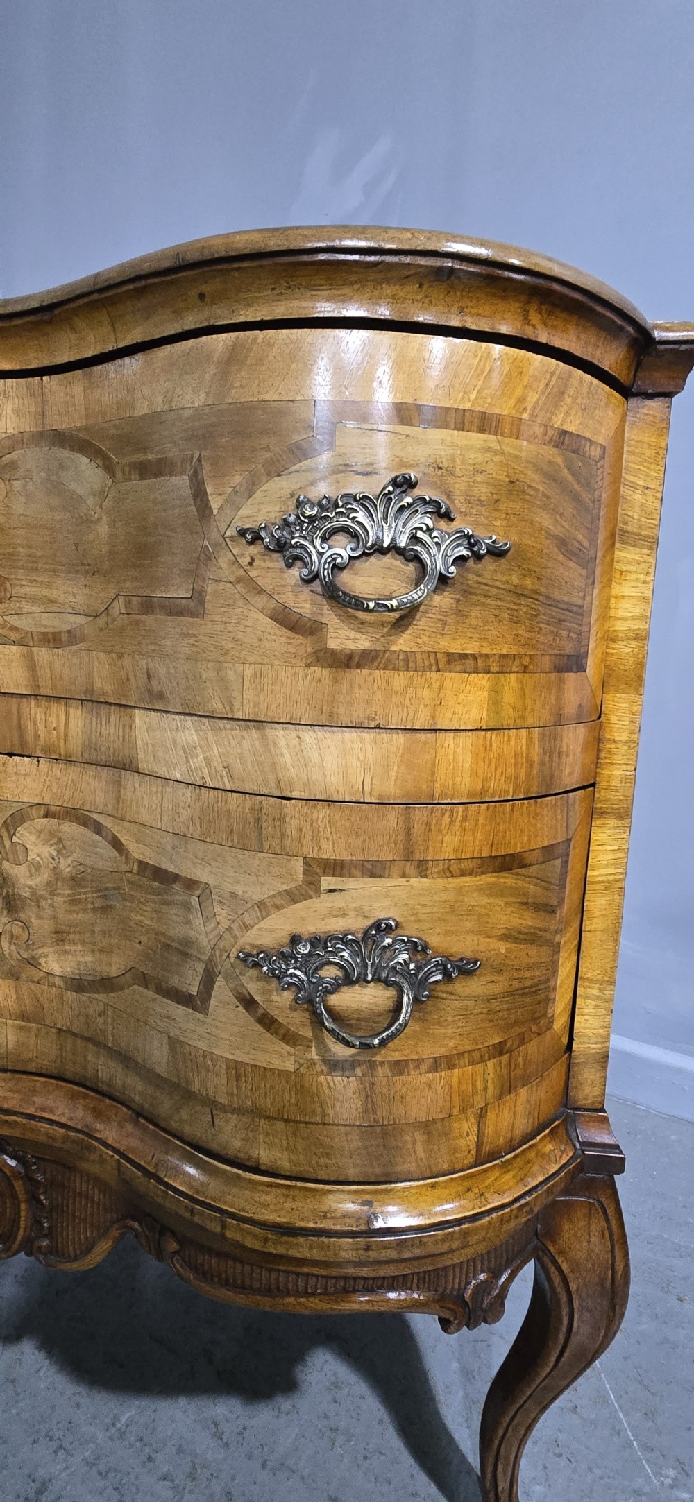 An antique walnut commode featuring two drawers with serpentine fronts, inlaid geometric banding, decorative brass handles, and carved cabriole legs. View V