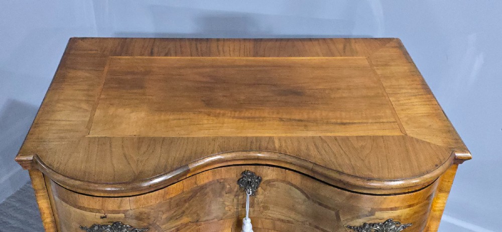 An antique walnut commode featuring two drawers with serpentine fronts, inlaid geometric banding, decorative brass handles, and carved cabriole legs. View VI