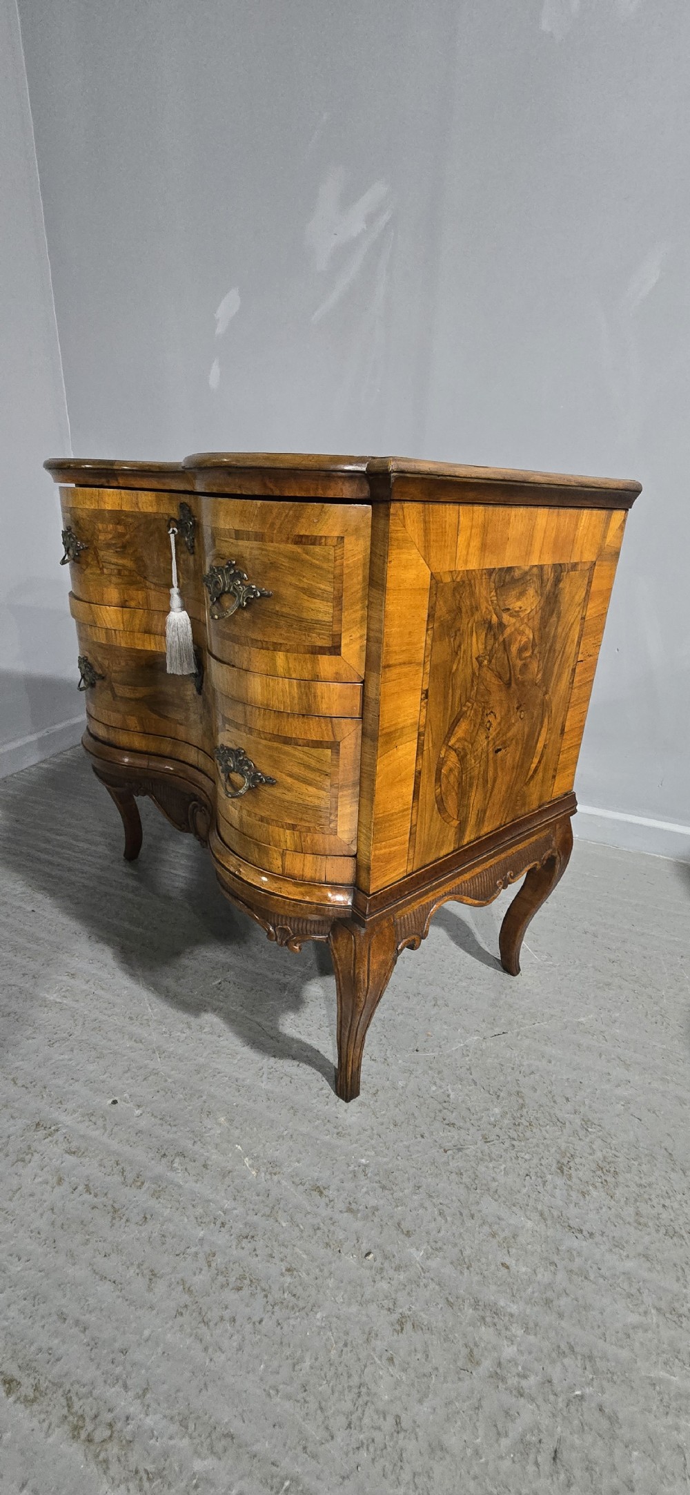 An antique walnut commode featuring two drawers with serpentine fronts, inlaid geometric banding, decorative brass handles, and carved cabriole legs. View XVI