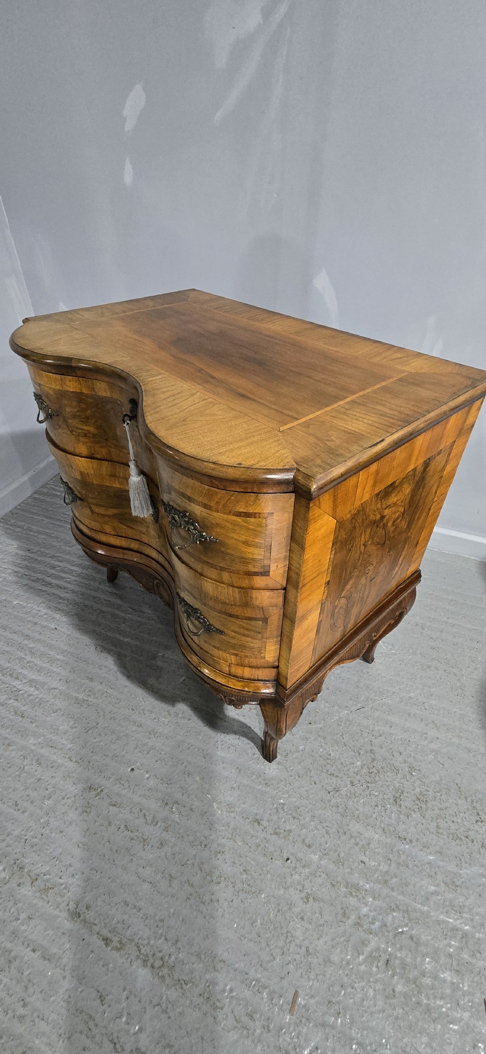 An antique walnut commode featuring two drawers with serpentine fronts, inlaid geometric banding, decorative brass handles, and carved cabriole legs. View XVII