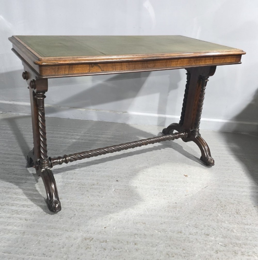 An antique Regency rosewood library writing table featuring a green leather inset top, barley twist supports, carved hipped feet, and a central twisted stretcher.