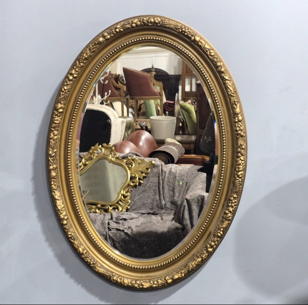 An oval wall mirror set in a gilded frame decorated with relief foliate patterns and beaded inner moulding.