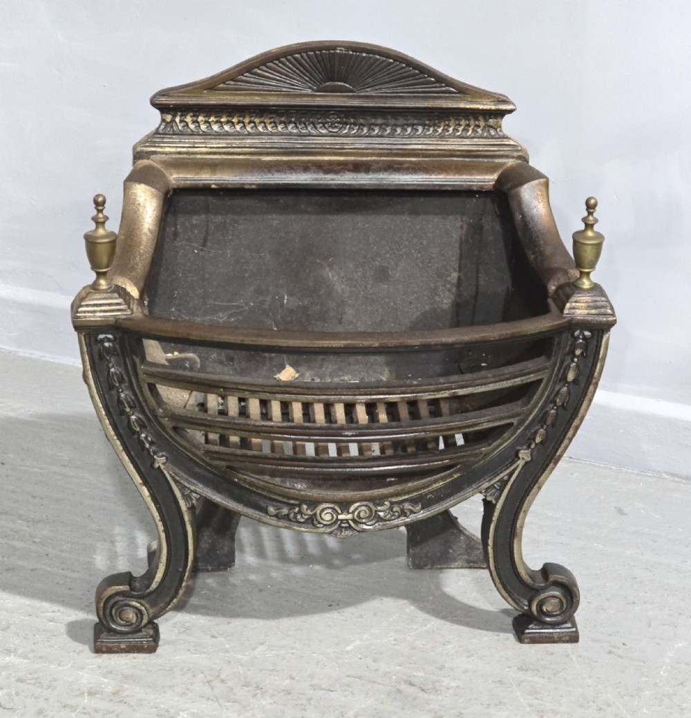 An antique Regency period cast iron fire grate featuring scrolled feet, brass urn finials, and a sunburst cresting.
