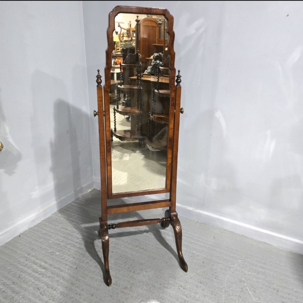 A freestanding burr walnut cheval mirror featuring a shaped arched top frame suspended between turned upright posts and supported on cabriole legs.