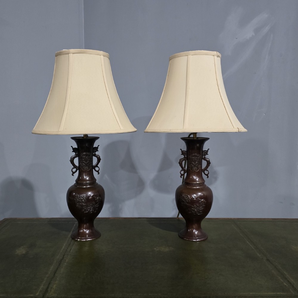 A pair of dark patinated Japanese bronze vase table lamps with dragon handles and flared cream fabric shades.