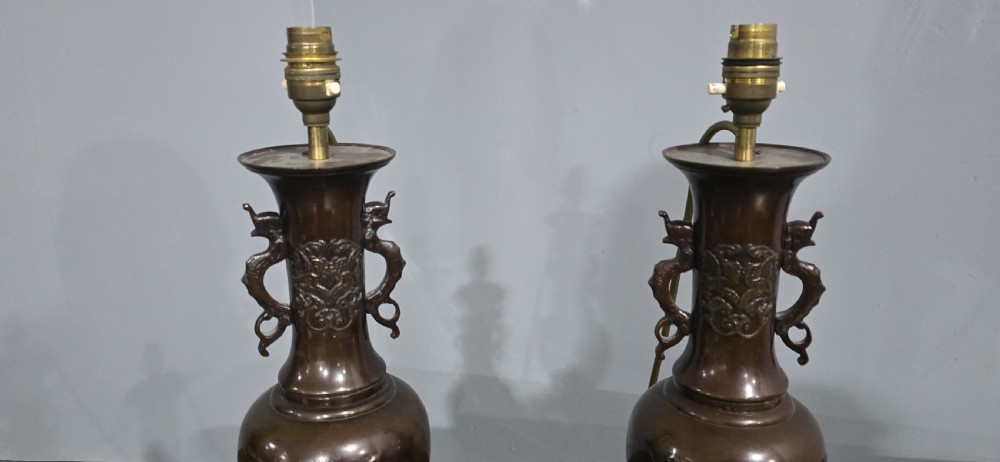 A pair of dark patinated Japanese bronze vase table lamps with dragon handles and flared cream fabric shades. View V