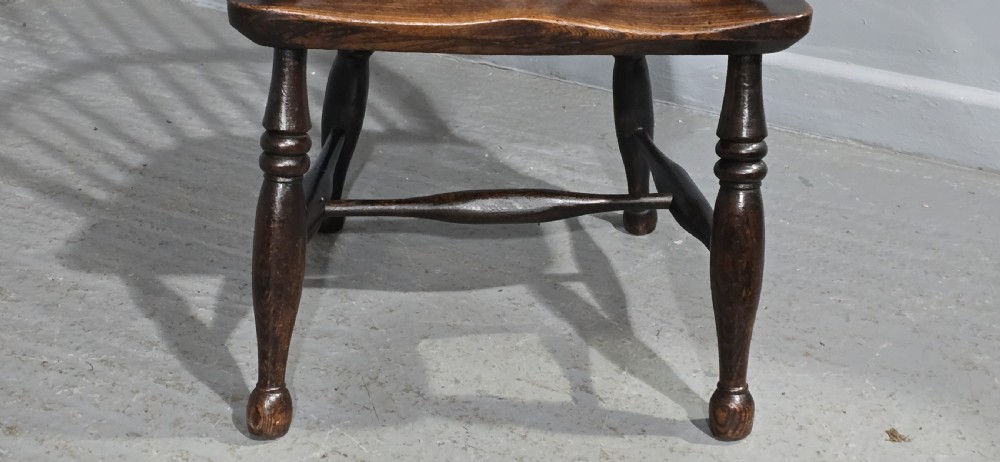 An antique dark brown timber Windsor armchair featuring a high hoop spindle back, curved armrests with turned supports, and a shaped solid wooden seat. View IV